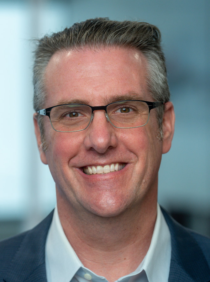 SVP of Operations for data centers at CEI, Adam smiles directly at the viewer. He wears glasses, a light blue dress shirt and navy jacket.