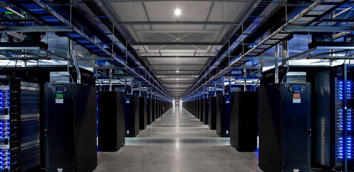 Perspective view looking between two rows of data center racks with blue lights flashing throughout.